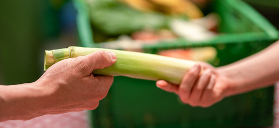 Übergabe von gerettetem Lauch zwischen zwei Personen als Symbolbild für die wertvolle finanzielle Unterstützung von den Spenderinnen und Spender an die karitative Foodsave-Organisation Tischlein deck dich, die gerettete Lebensmittel an armutsbetroffene Menschen abgibt.