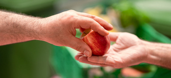 Übergabe eines geretteten Apfels zwischen zwei Personen als Symbolbild für die wertvolle finanzielle Unterstützung von den Spenderinnen und Spender an die karitative Foodsave-Organisation Tischlein deck dich, die gerettete Lebensmittel an armutsbetroffene Menschen abgibt.