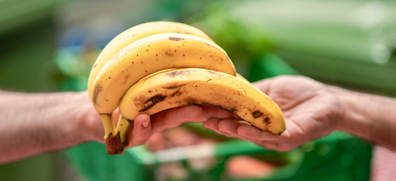 Übergabe einer geretteten Banane zwischen zwei Personen als Symbolbild für die wertvolle finanzielle Unterstützung von den Spenderinnen und Spender an die karitative Foodsave-Organisation Tischlein deck dich, die gerettete Lebensmittel an armutsbetroffene Menschen abgibt.