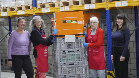 Mitarbeitende und Freiwillige von Tischlein deck dich im Logistiklager Winterthur umgeben von Paletten mit gespendeten Lebensmitteln, die an den Tischlein deck dich-Abgabestellen verteilt werden. 