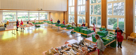 Innenansicht der Abgabestelle Chur Comander der Hilfsorganisation Tischlein deck dich, wo freiwillige Helferinnen gerettete Lebensmittel auf Tischen für armutsbetroffene Menschen bereitstellen.