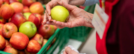 Freiwillige Helferin der Hilfsorganisation Tischlein deck dich übergibt einen geretteten Apfel an eine armutsbetroffene Person.