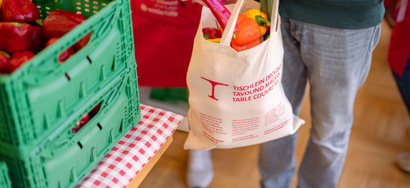 Freiwillige Helferin legt an einer Abgabestelle der Hilfsorganisation Tischlein deck dich einer armutsbetroffenen Person gerettetes Gemüse in die Tasche und leistet so einen Beitrag für die Lebensmittelhilfe.
