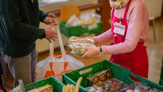 Freiwillige Helferin der Hilfsorganisation Tischlein deck dich verteilt gerettete Champignons an eine armutsbetroffene Kundin und trägt so zur Lebensmittelhilfe in der Schweiz bei.